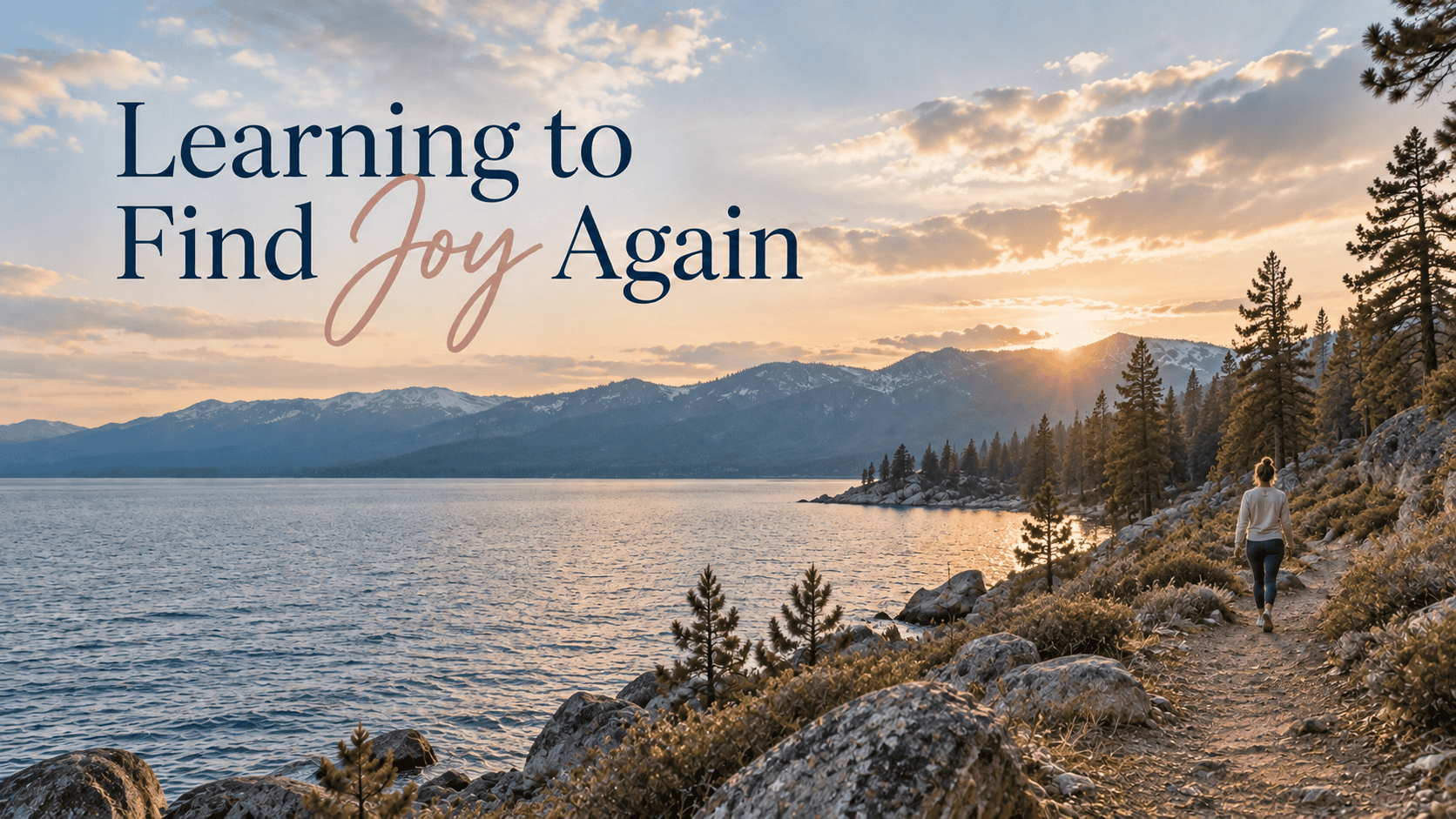Woman walking along rocky lakeshore at sunset with mountains and trees.
